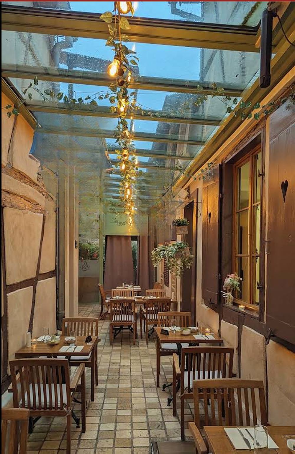 La salle sous verriere, tables dressees et guirlande lumineuse